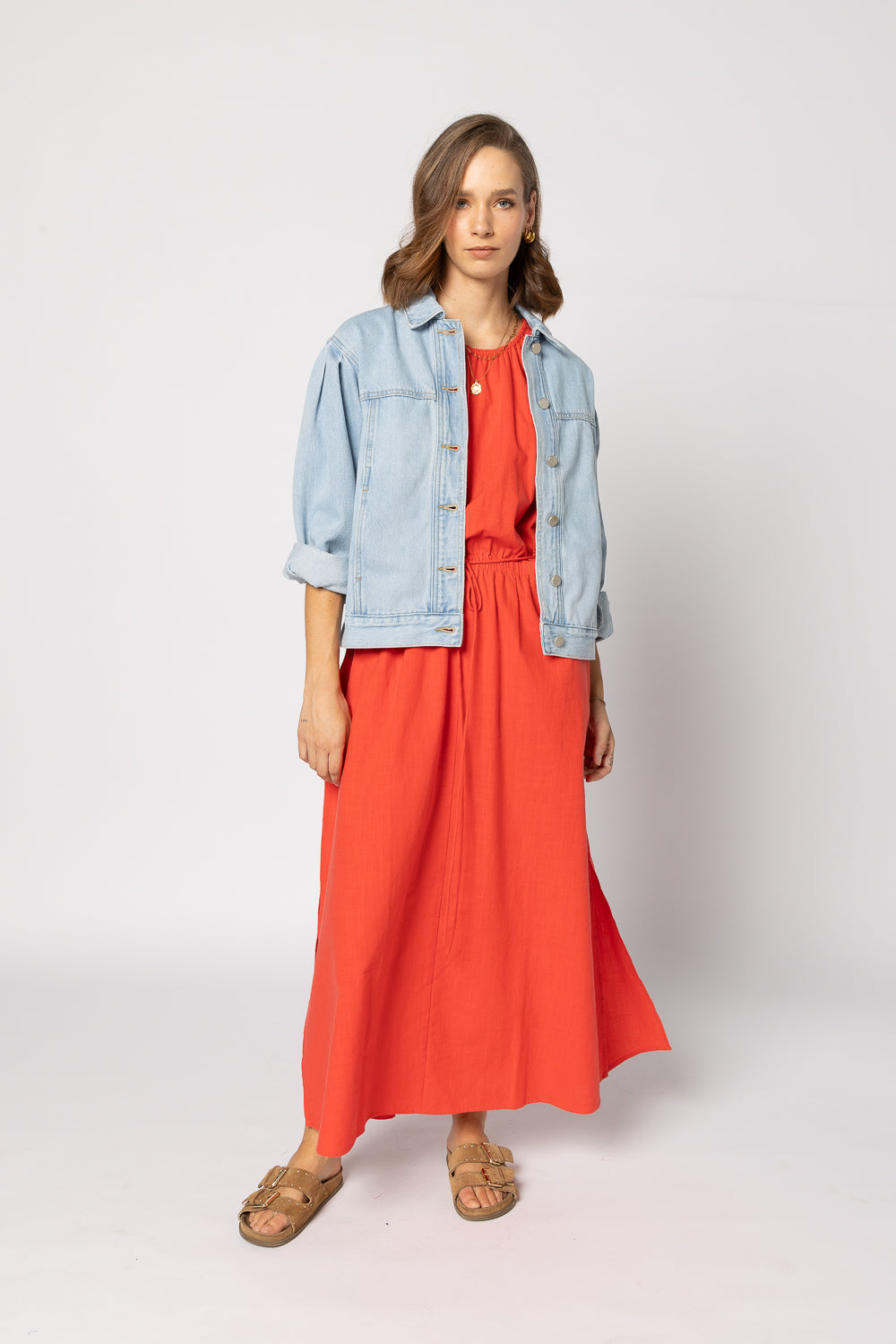 Woman wearing a red dress with a light blue denim jacket on a white background